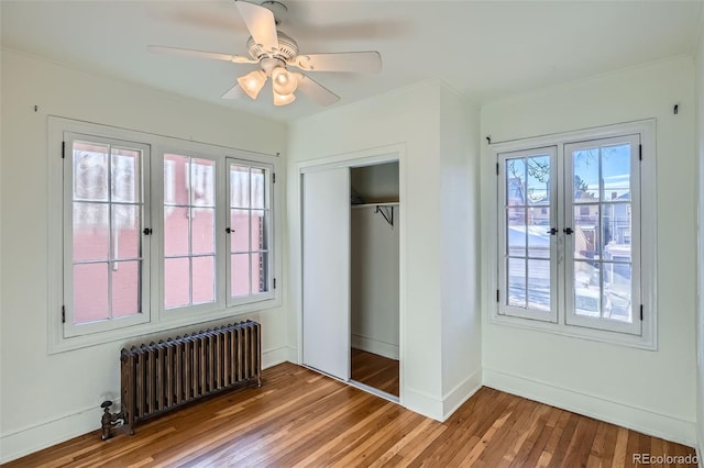 unfurnished bedroom featuring ceiling fan, multiple windows, hardwood / wood-style flooring, radiator, and a closet