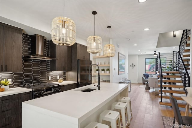 kitchen with an island with sink, sink, decorative backsplash, range, and wall chimney exhaust hood