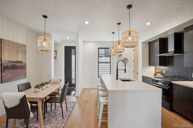 kitchen with wall chimney exhaust hood, sink, black gas range oven, a kitchen island with sink, and decorative backsplash