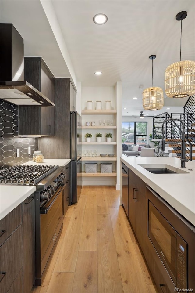 kitchen with wall chimney range hood, dark brown cabinets, light hardwood / wood-style flooring, and stainless steel appliances