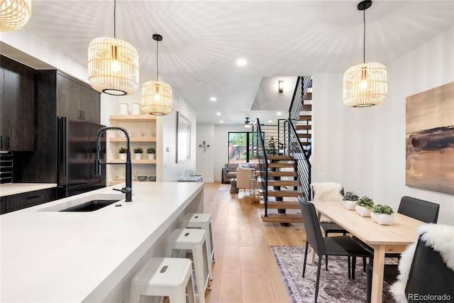 kitchen with black refrigerator, decorative light fixtures, sink, dark brown cabinetry, and light hardwood / wood-style floors