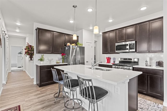 kitchen with pendant lighting, stainless steel appliances, tasteful backsplash, sink, and a kitchen island with sink