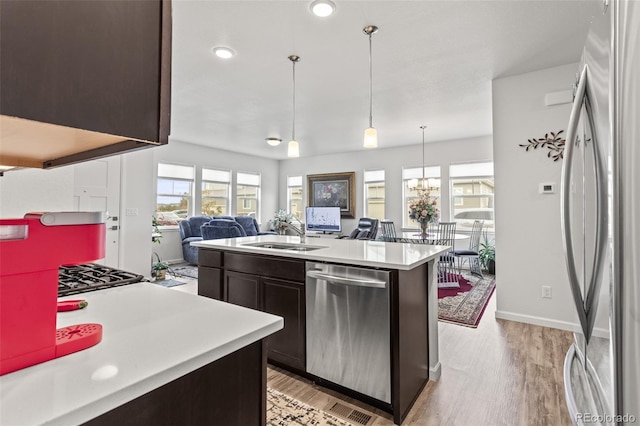 kitchen featuring sink, decorative light fixtures, stainless steel appliances, an island with sink, and dark brown cabinetry