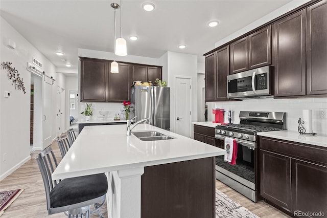 kitchen featuring appliances with stainless steel finishes, a barn door, sink, pendant lighting, and an island with sink