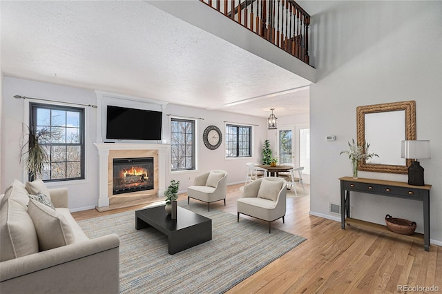 living area with baseboards, a fireplace, light wood-style flooring, and a textured ceiling