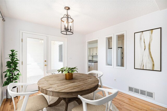 dining space with french doors, light wood finished floors, visible vents, a textured ceiling, and a chandelier