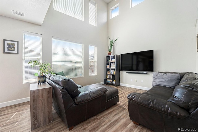 living area with a high ceiling, visible vents, baseboards, and wood finished floors