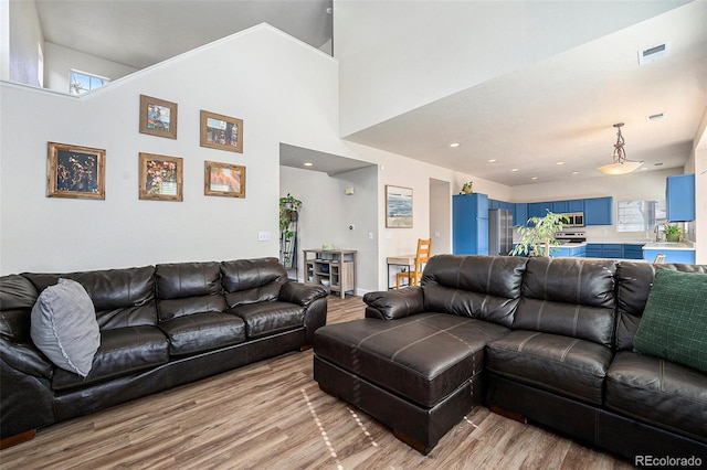 living room with light wood-type flooring, a towering ceiling, and visible vents