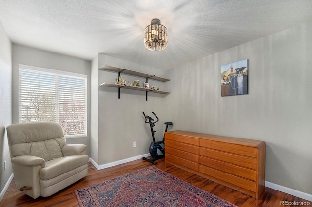 living area featuring a notable chandelier, a textured ceiling, baseboards, and wood finished floors