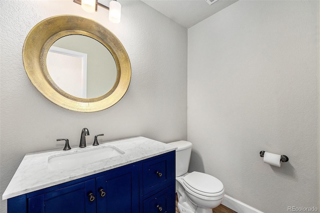 bathroom with toilet, a textured wall, baseboards, and vanity