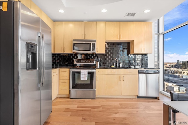 kitchen with decorative backsplash, light brown cabinets, light wood-type flooring, and appliances with stainless steel finishes