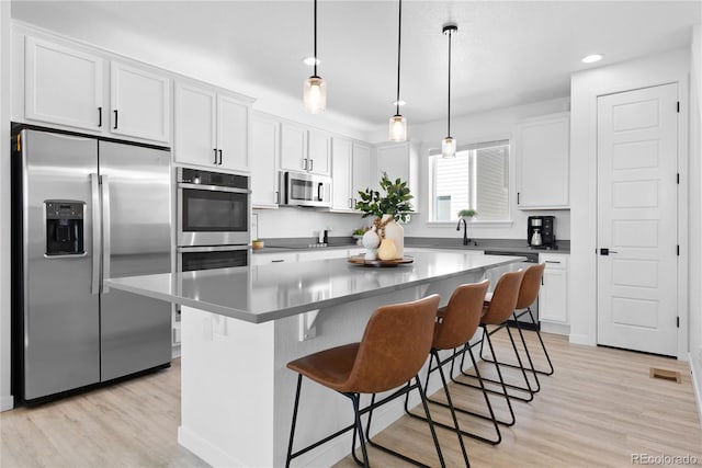 12261 Farmview St, Thornton, CO 80241 - kitchen with stainless steel appliances, white cabinets, light wood-type flooring, a breakfast bar area, and recessed lighting