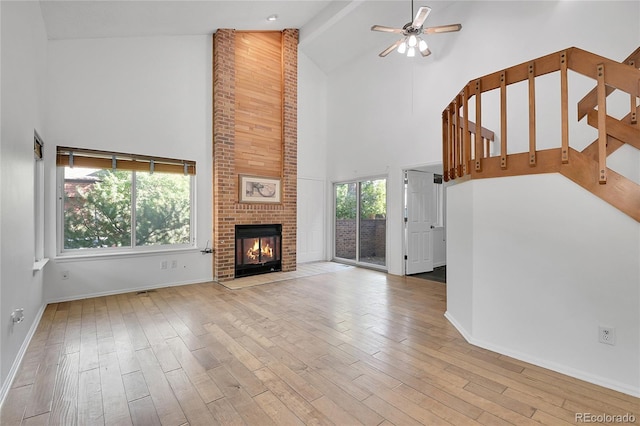 unfurnished living room with high vaulted ceiling, a brick fireplace, light hardwood / wood-style floors, and a healthy amount of sunlight