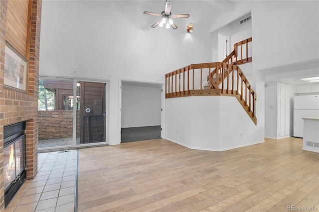 unfurnished living room with ceiling fan, light wood-type flooring, a fireplace, and high vaulted ceiling