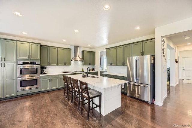 26591 E Calhoun Pl, Aurora, CO 80016 - kitchen featuring appliances with stainless steel finishes, green cabinetry, wall chimney exhaust hood, dark wood-style floors, and recessed lighting