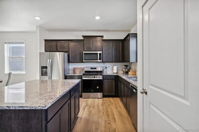 kitchen featuring light wood-style flooring, dark brown cabinetry, stainless steel appliances, light stone countertops, and tasteful backsplash