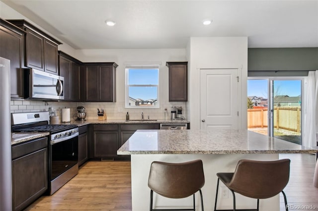 kitchen with a breakfast bar, a kitchen island, dark brown cabinets, appliances with stainless steel finishes, and tasteful backsplash