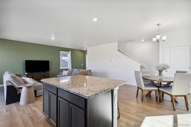 kitchen with light wood finished floors, recessed lighting, a kitchen island, light stone countertops, and a chandelier