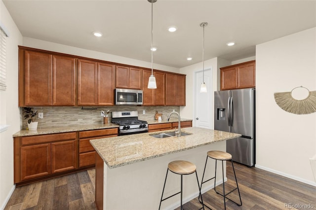 kitchen featuring light stone countertops, appliances with stainless steel finishes, sink, pendant lighting, and an island with sink