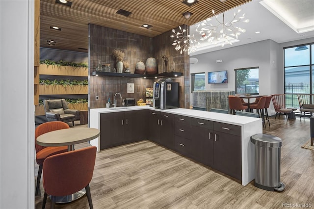 kitchen with dark brown cabinetry, sink, pendant lighting, wooden ceiling, and light hardwood / wood-style floors