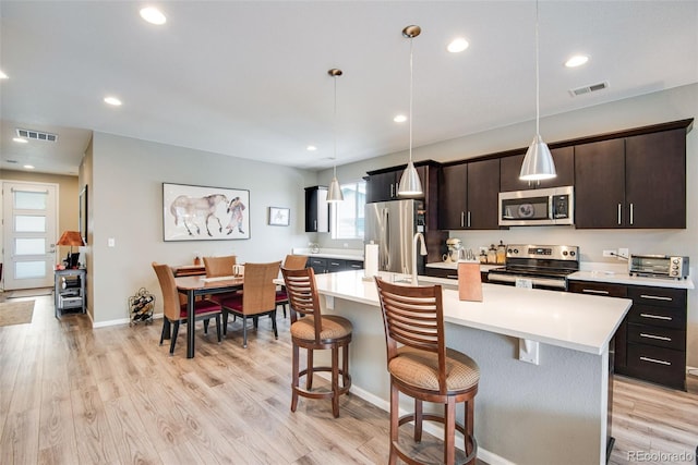 3022 Merlin Dr, Brighton, CO 80601 - kitchen with stainless steel appliances, a breakfast bar area, light countertops, a center island with sink, and light wood finished floors