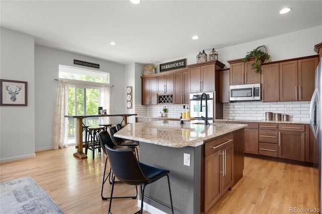 15502 E Flower Mound Pl, Parker, CO 80134 - kitchen featuring appliances with stainless steel finishes, a center island, a breakfast bar, light wood-style flooring, and decorative backsplash
