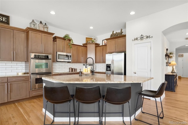 15502 E Flower Mound Pl, Parker, CO 80134 - kitchen featuring stainless steel appliances, a breakfast bar area, arched walkways, light wood-style flooring, and tasteful backsplash