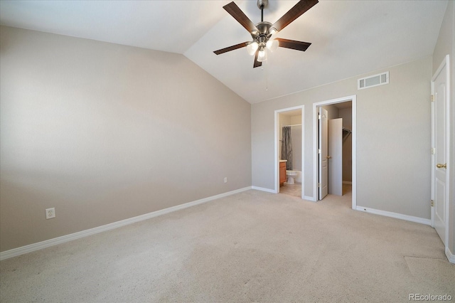 unfurnished bedroom featuring ceiling fan, ensuite bathroom, light colored carpet, a walk in closet, and a closet