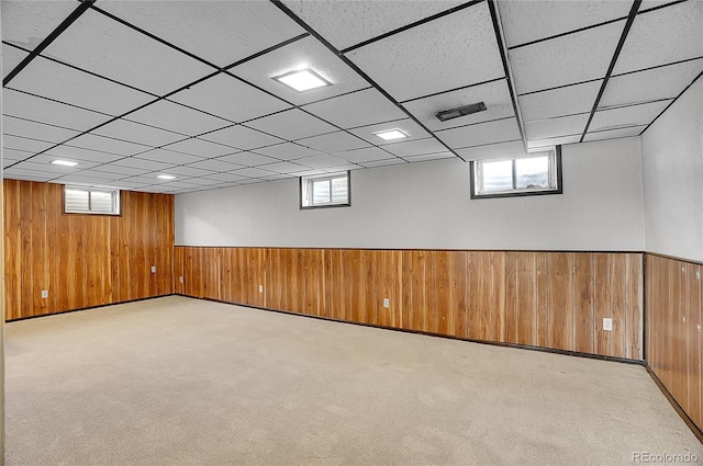 basement featuring wooden walls, light colored carpet, wainscoting, and a wealth of natural light