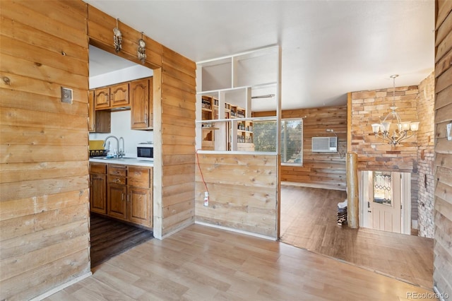 kitchen with kitchen peninsula, wood walls, hanging light fixtures, and light hardwood / wood-style floors