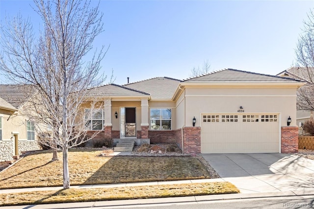 prairie-style house featuring driveway, brick siding, an attached garage, and stucco siding