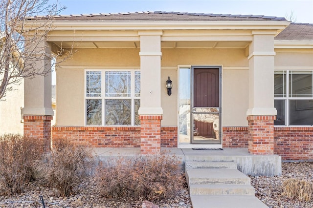 view of exterior entry featuring brick siding, a porch, and stucco siding