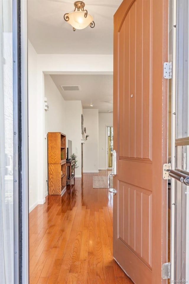 hallway featuring arched walkways, light wood finished floors, visible vents, and baseboards