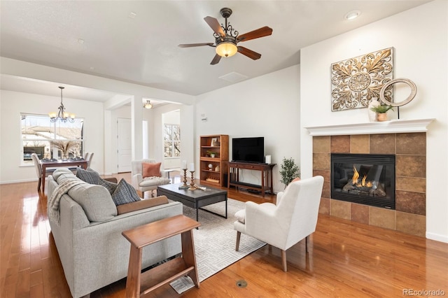 living room featuring ceiling fan with notable chandelier, a fireplace, baseboards, and wood finished floors