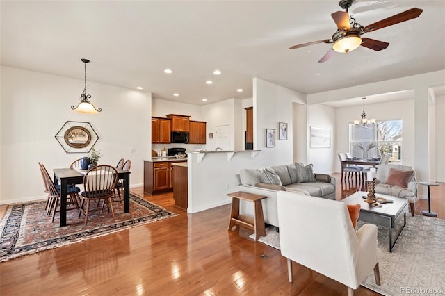 living room with ceiling fan with notable chandelier, baseboards, hardwood / wood-style floors, and recessed lighting