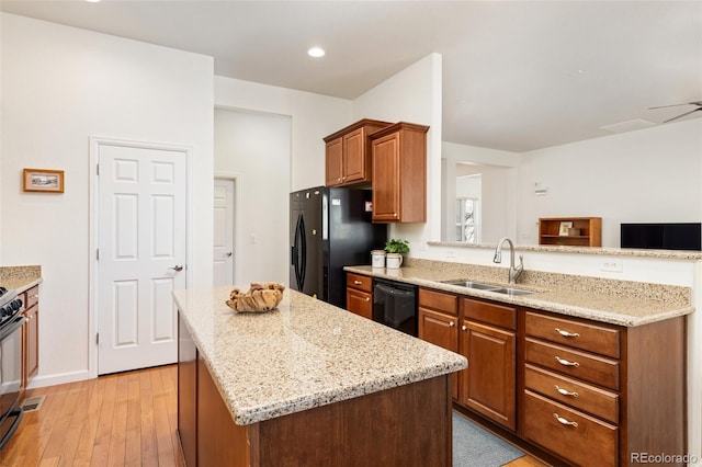 kitchen featuring black appliances, light stone counters, a sink, and a center island