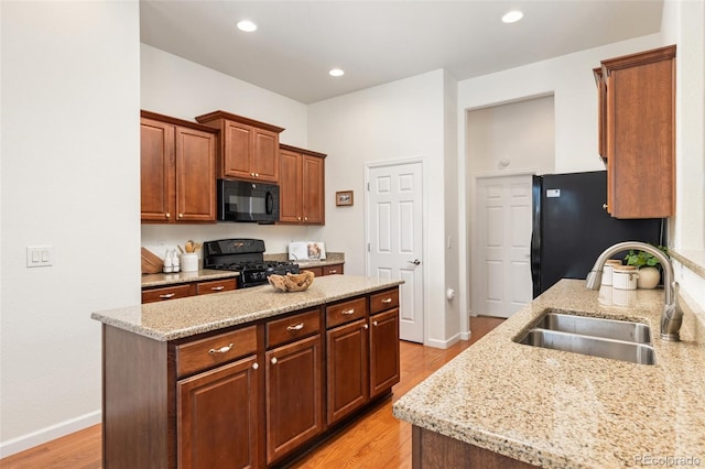 kitchen with black appliances, light stone counters, a sink, and light wood-style floors