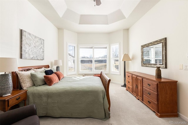 bedroom with light carpet, a raised ceiling, a ceiling fan, and baseboards