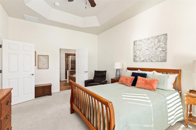 bedroom with ceiling fan, light colored carpet, a high ceiling, a raised ceiling, and ensuite bath