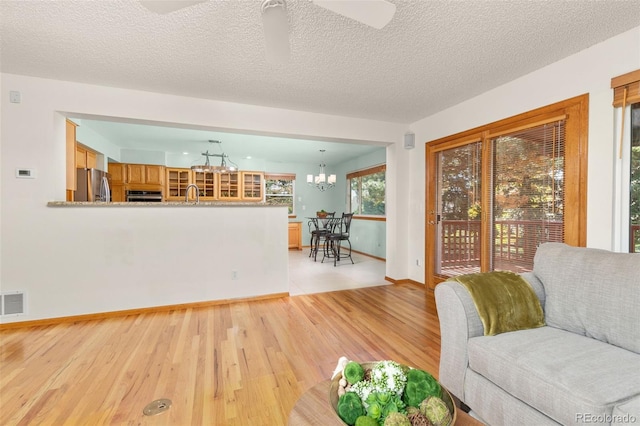 unfurnished living room with sink, ceiling fan with notable chandelier, light hardwood / wood-style flooring, and a textured ceiling