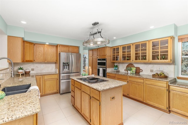 kitchen with sink, light stone counters, hanging light fixtures, appliances with stainless steel finishes, and a kitchen island