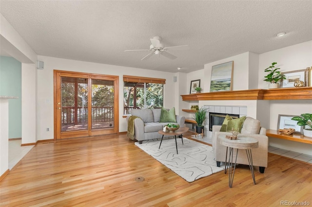 living room featuring a tiled fireplace, a textured ceiling, and light wood-type flooring