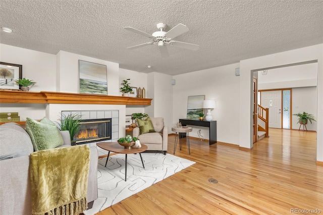 living room featuring ceiling fan, a fireplace, light hardwood / wood-style flooring, and a textured ceiling