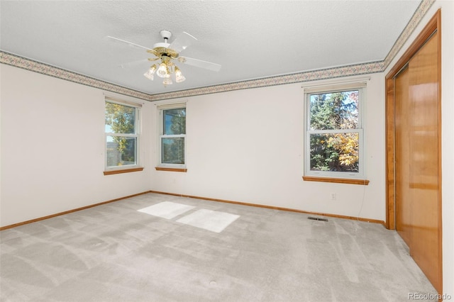 carpeted empty room featuring crown molding, plenty of natural light, a textured ceiling, and ceiling fan