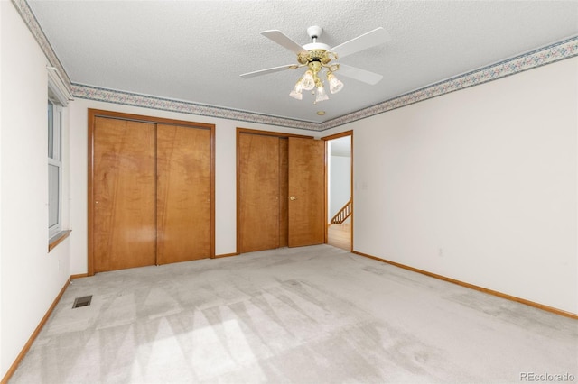 unfurnished bedroom with multiple closets, ceiling fan, light colored carpet, and a textured ceiling