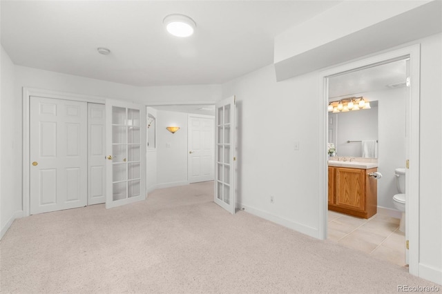 unfurnished bedroom with french doors, light colored carpet, ensuite bath, and a closet