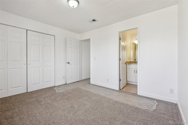 unfurnished bedroom featuring ensuite bathroom, light colored carpet, a closet, and a textured ceiling