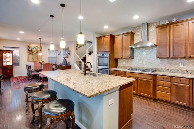 2415 Bluestem Willow Dr, Loveland, CO 80538 - kitchen featuring wall chimney exhaust hood, stainless steel appliances, a sink, a kitchen breakfast bar, and brown cabinetry