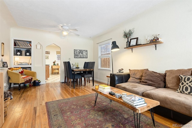 living room featuring light wood-style floors, arched walkways, baseboards, and a ceiling fan