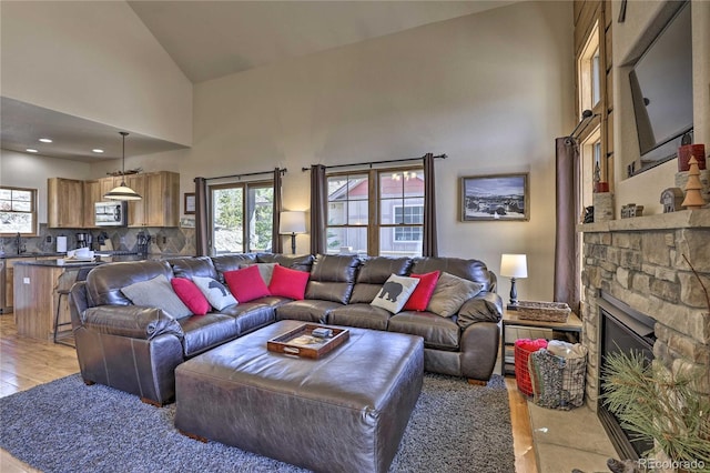 living area with light wood-style flooring, a fireplace, and high vaulted ceiling